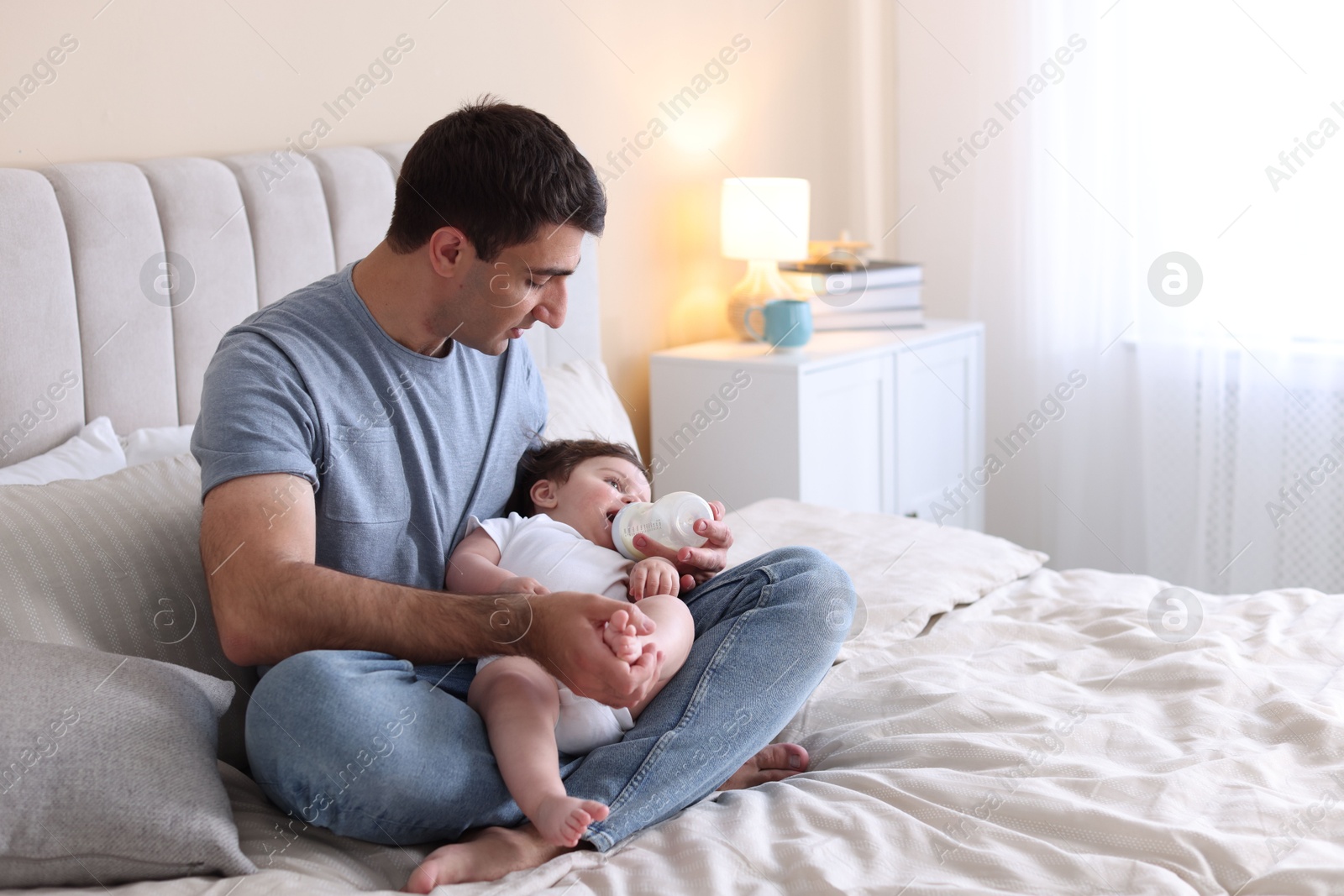 Father feeding his little baby with bottle on bed at home. Space for text Photo of Father feeding his little baby with bottle on bed at home. Space for text