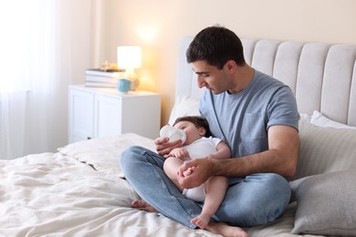 Photo of Father feeding his little baby with bottle on bed at home. Space for text
