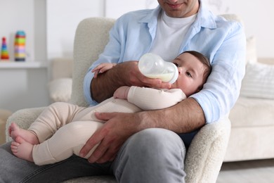 Photo of Father feeding his little baby with bottle on armchair at home, closeup