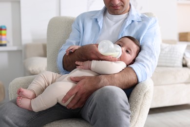 Photo of Father feeding his little baby with bottle on armchair at home, closeup