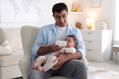 Photo of Father feeding his little baby with bottle on armchair at home