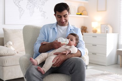 Photo of Father feeding his little baby with bottle on armchair at home