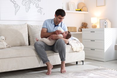 Photo of Father feeding his little baby with bottle on sofa at home