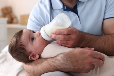 Photo of Father feeding his little baby with bottle on sofa at home, closeup
