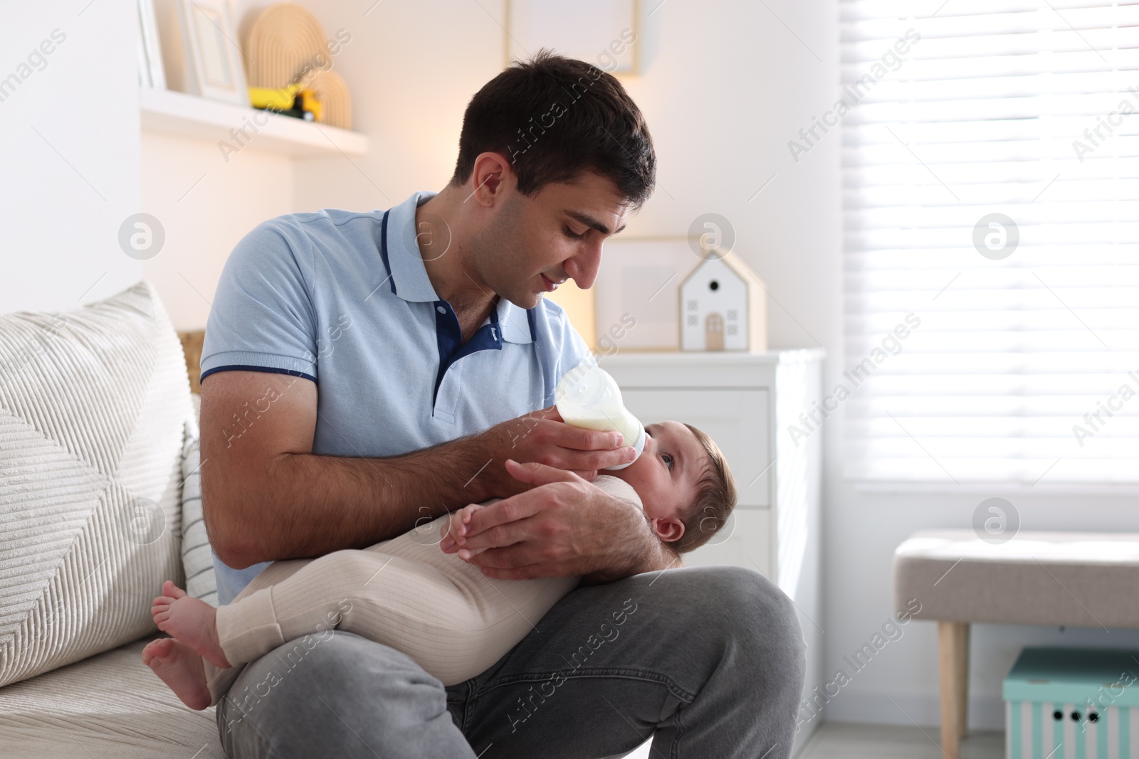 Father feeding his little baby with bottle on sofa at home. Space for text Photo of Father feeding his little baby with bottle on sofa at home. Space for text