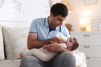 Photo of Father feeding his little baby with bottle on sofa at home