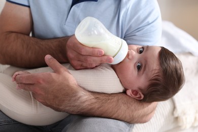 Photo of Father feeding his little baby with bottle on sofa at home, closeup