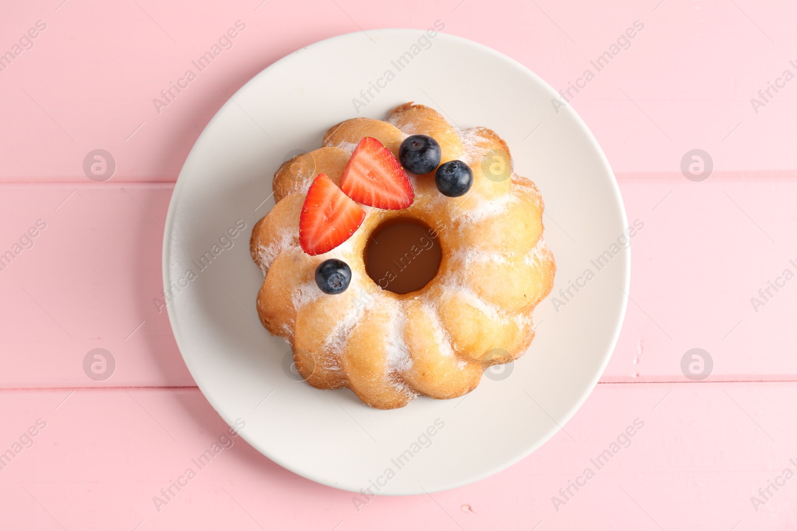 Tasty Bundt cake with powdered sugar and berries on pink wooden table, top view. Photo of Tasty Bundt cake with powdered sugar and berries on pink wooden table, top view.