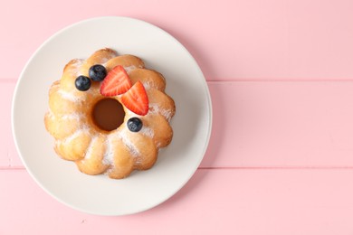 Photo of Tasty Bundt cake with powdered sugar and berries on pink wooden table, top view. Space for text