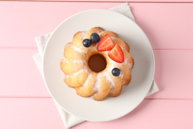 Photo of Tasty Bundt cake with powdered sugar and berries on pink wooden table, top view.