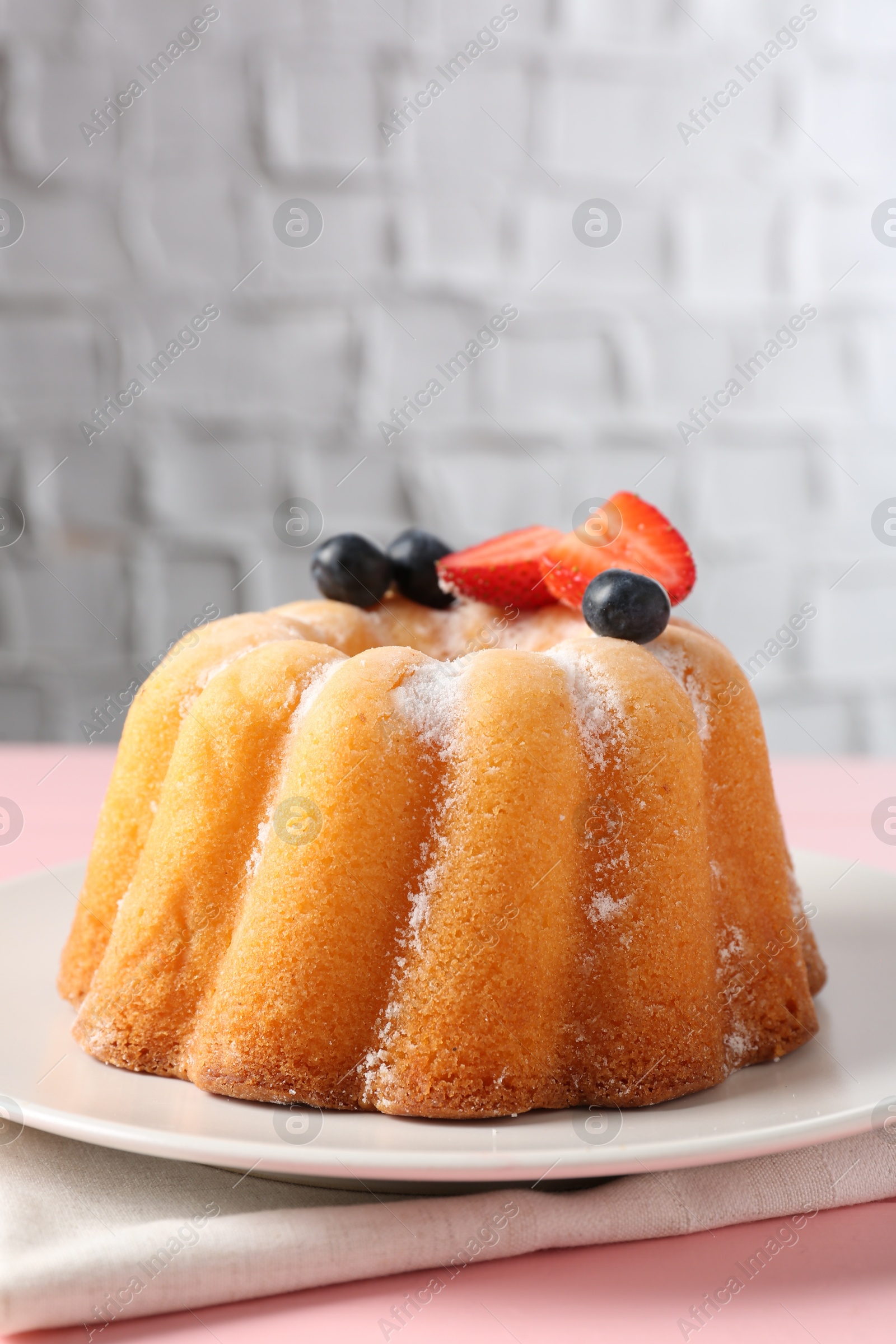 Tasty Bundt cake with powdered sugar and berries on pink wooden table, closeup Photo of Tasty Bundt cake with powdered sugar and berries on pink wooden table, closeup