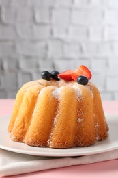 Photo of Tasty Bundt cake with powdered sugar and berries on pink wooden table, closeup