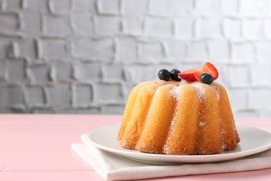 Photo of Tasty Bundt cake with powdered sugar and berries on pink wooden table, closeup. Space for text