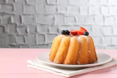 Photo of Tasty Bundt cake with powdered sugar and berries on pink wooden table, closeup. Space for text
