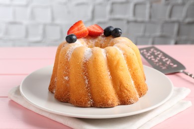 Photo of Tasty Bundt cake with powdered sugar, berries and server on pink wooden table, closeup