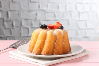 Photo of Tasty Bundt cake with powdered sugar, berries and server on pink wooden table, closeup