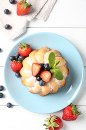 Photo of Tasty Bundt cake with powdered sugar and berries on white wooden table, flat lay