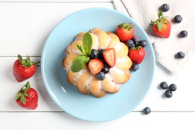 Photo of Tasty Bundt cake with powdered sugar and berries on white wooden table, flat lay