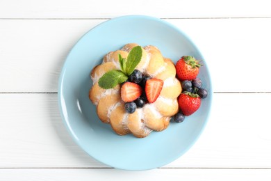 Photo of Tasty Bundt cake with powdered sugar and berries on white wooden table, top view