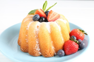 Photo of Tasty Bundt cake with powdered sugar and berries on white table, closeup