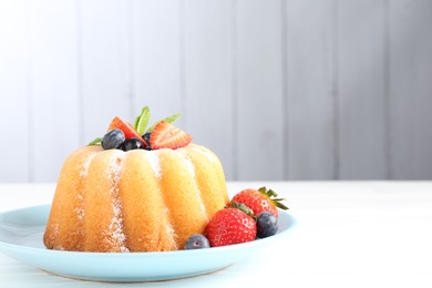 Photo of Tasty Bundt cake with powdered sugar and berries on white wooden table, closeup. Space for text