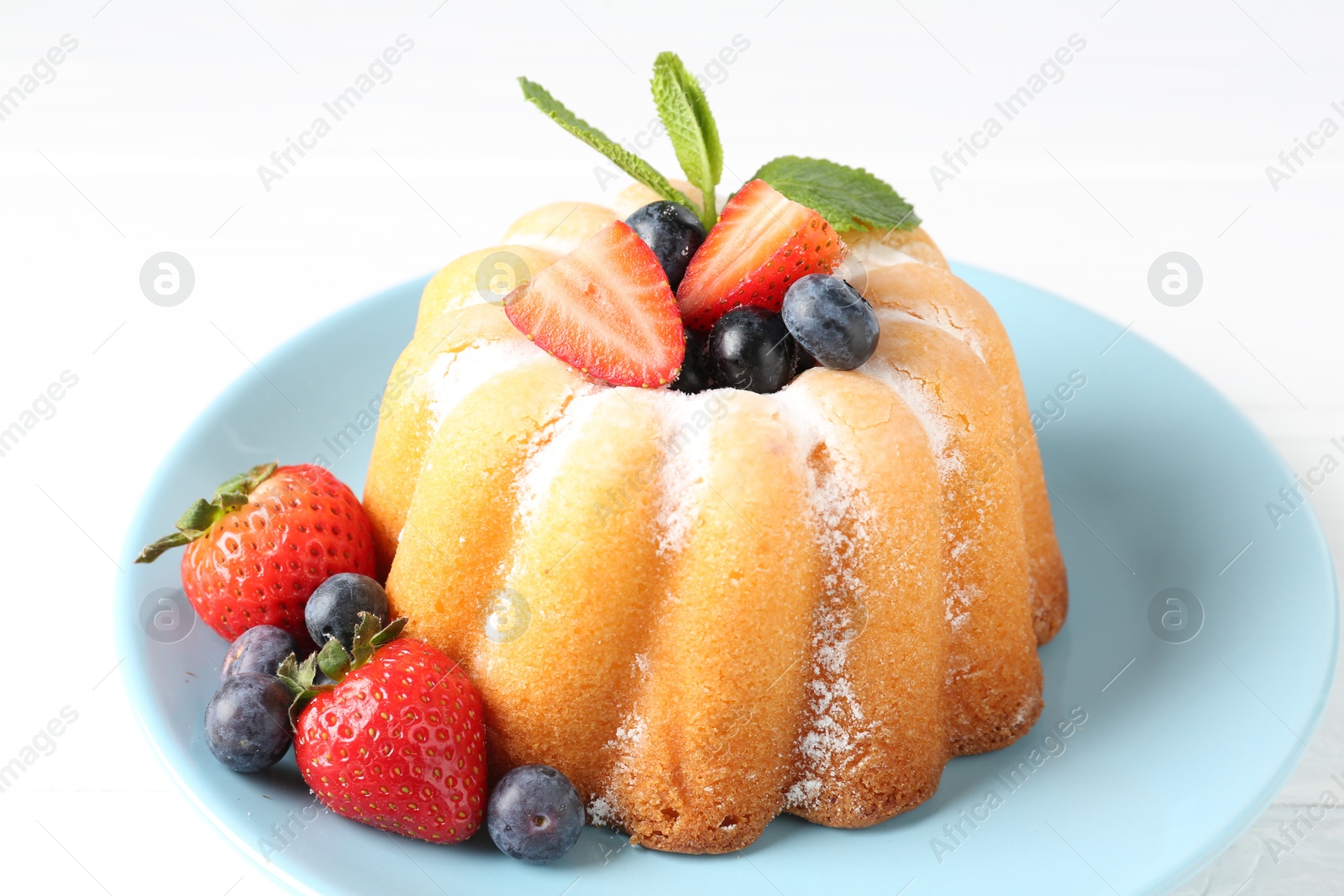 Tasty Bundt cake with powdered sugar and berries on white table, closeup Photo of Tasty Bundt cake with powdered sugar and berries on white table, closeup