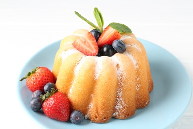Photo of Tasty Bundt cake with powdered sugar and berries on white table, closeup