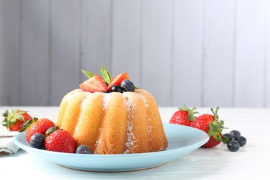 Photo of Tasty Bundt cake with powdered sugar and berries on white wooden table, closeup