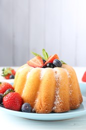 Photo of Tasty Bundt cake with powdered sugar and berries on white wooden table, closeup. Space for text