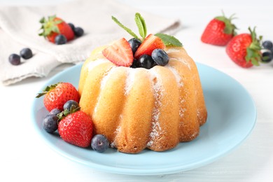 Photo of Tasty Bundt cake with powdered sugar and berries on white wooden table, closeup