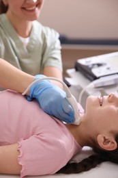 Photo of Sonographer conducting girl's thyroid gland ultrasound examination in clinic, closeup