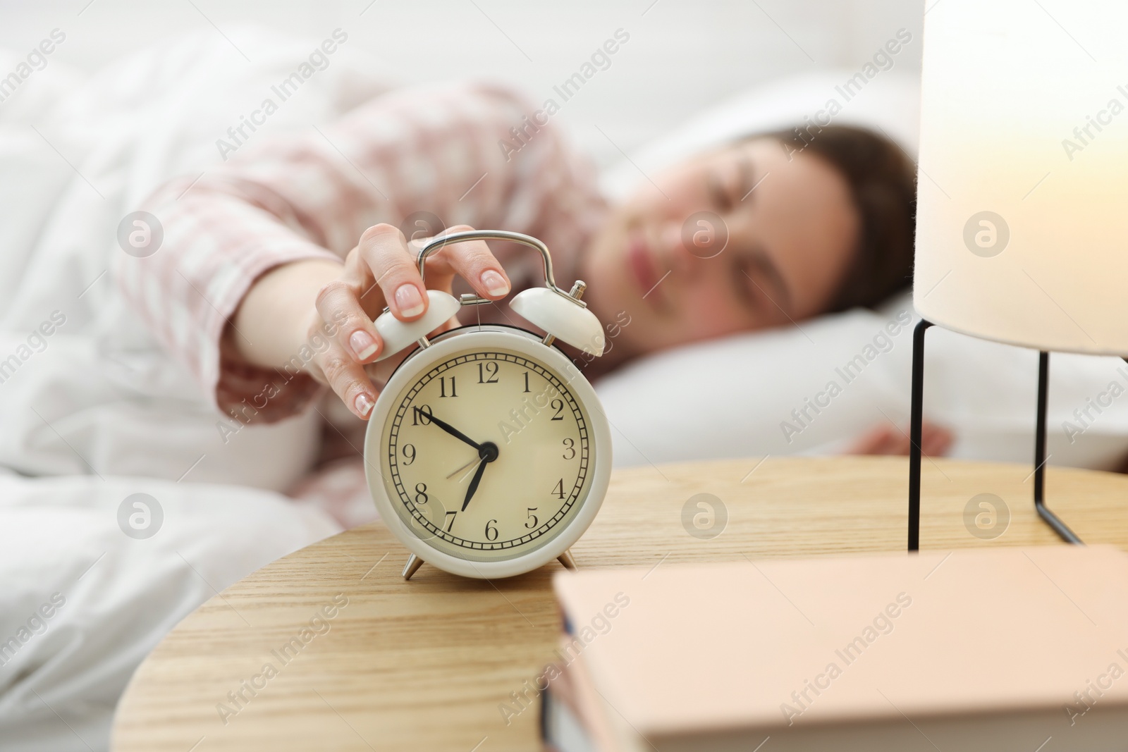 Young woman turning off alarm clock at home, selective focus Photo of Young woman turning off alarm clock at home, selective focus