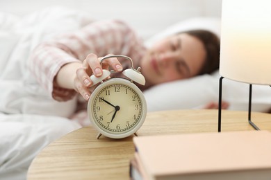 Photo of Young woman turning off alarm clock at home, selective focus