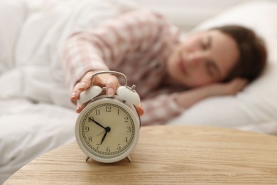Photo of Young woman turning off alarm clock at home, selective focus
