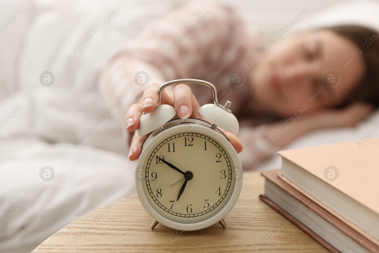 Young woman turning off alarm clock at home, selective focus Photo of Young woman turning off alarm clock at home, selective focus