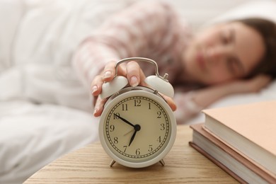 Photo of Young woman turning off alarm clock at home, selective focus