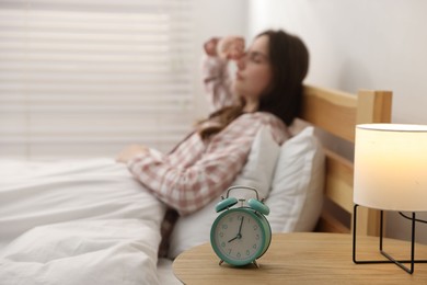 Photo of Young woman on bed indoors, focus on alarm clock