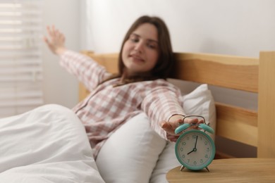 Photo of Young woman stretching and turning off alarm clock on bed at home, selective focus