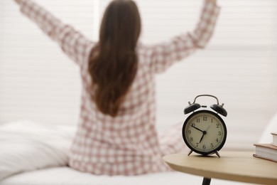 Photo of Young woman stretching on bed at home, focus on alarm clock