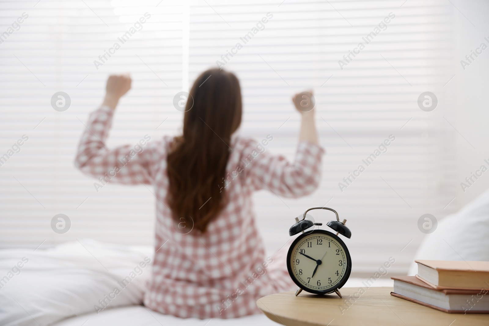 Young woman stretching on bed at home, focus on alarm clock Photo of Young woman stretching on bed at home, focus on alarm clock