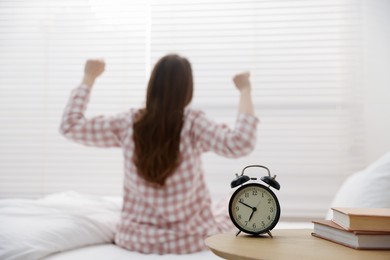 Photo of Young woman stretching on bed at home, focus on alarm clock