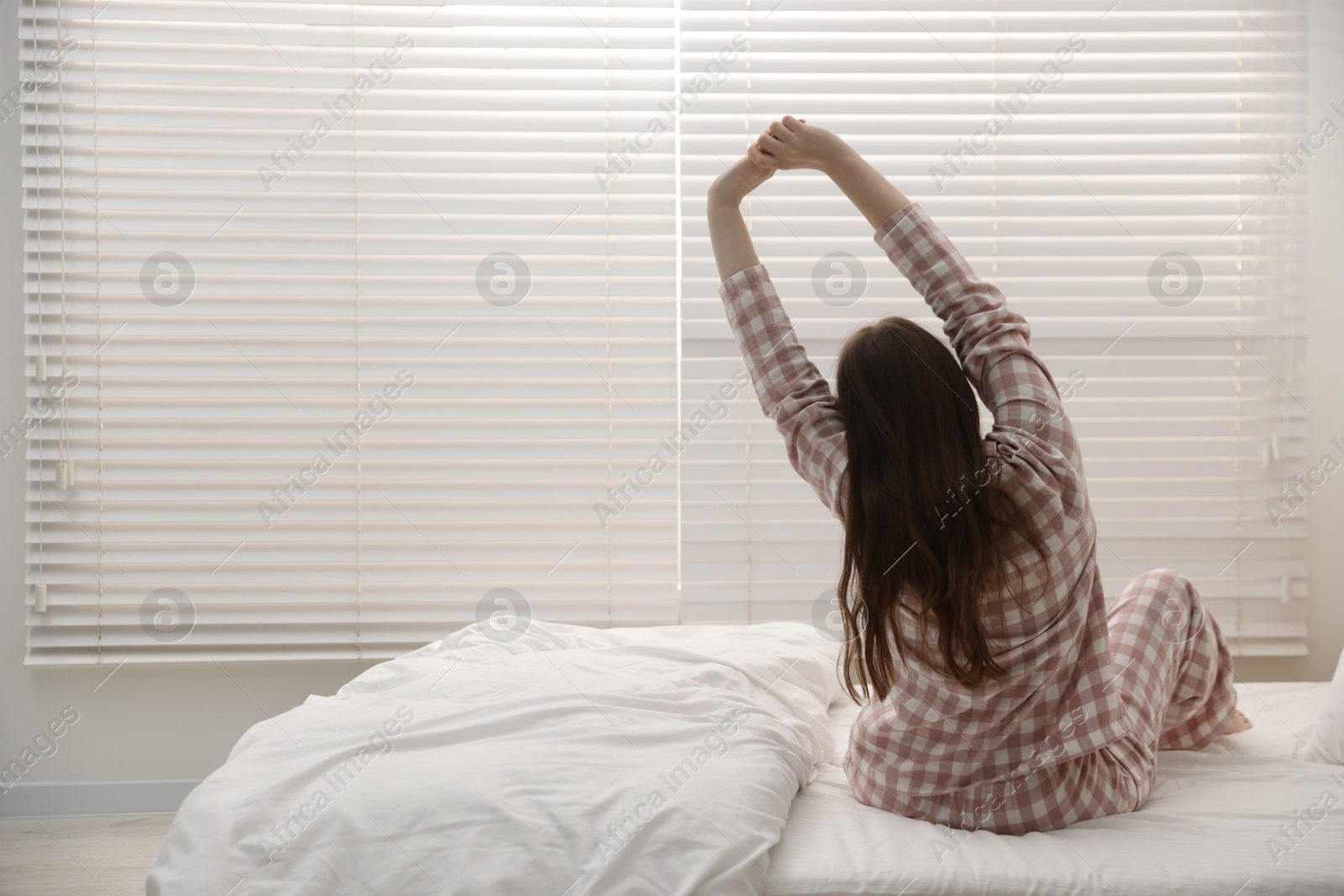 Young woman stretching on bed at home, back view. Space for text Photo of Young woman stretching on bed at home, back view. Space for text
