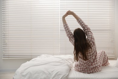 Photo of Young woman stretching on bed at home, back view. Space for text