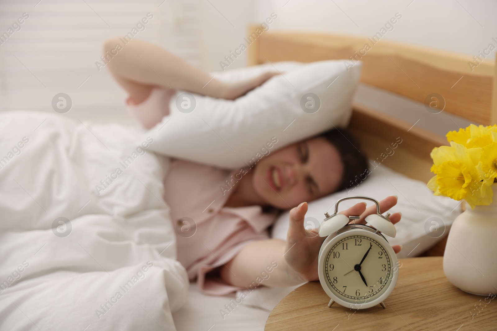 Frustrated young woman covering ears with pillow and turning off alarm clock on bed at home, selective focus Photo of Frustrated young woman covering ears with pillow and turning off alarm clock on bed at home, selective focus