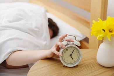 Photo of Woman turning off alarm clock on bed at home, selective focus