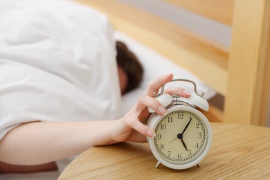Photo of Woman turning off alarm clock on bed at home, selective focus