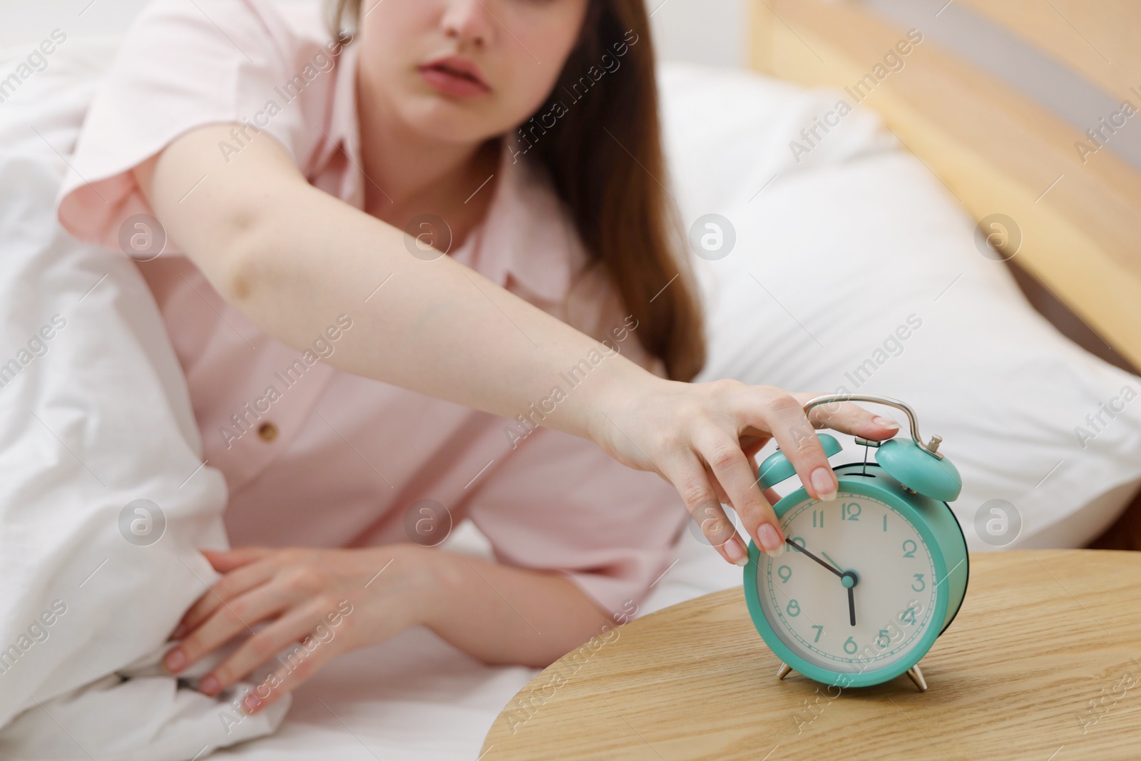 Woman turning off alarm clock on bed at home, selective focus Photo of Woman turning off alarm clock on bed at home, selective focus