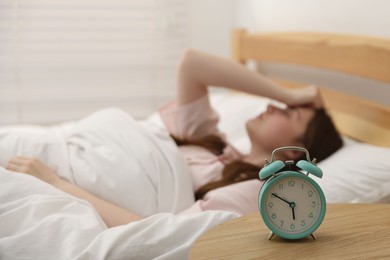 Photo of Frustrated young woman on bed at home, focus on alarm clock
