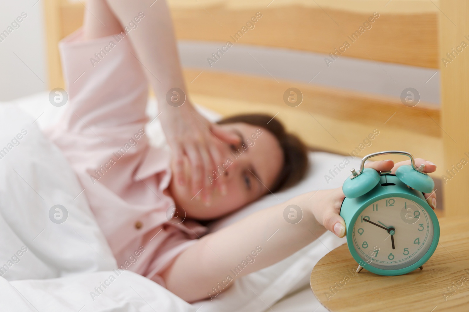 Frustrated young woman turning off alarm clock on bed at home, selective focus Photo of Frustrated young woman turning off alarm clock on bed at home, selective focus