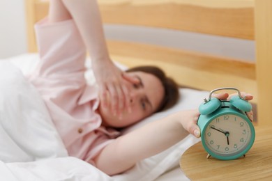 Photo of Frustrated young woman turning off alarm clock on bed at home, selective focus